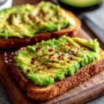 Nahaufnahme von 5-Minuten Avocado Brot mit geschnittenem Avocado, Salz und Chiliflocken auf einem Holzbrett.
