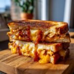 Gestapelte BBQ H&auml;hnchen Grilled Cheese Sandwiches mit geschmolzenem K&auml;se auf einem Holzbrett.