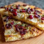 Nahaufnahme von zwei Scheiben Birnen-, Brie- & Cranberry-Flammkuchen mit Thymian auf einem Holzbrett.