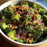 Nahaufnahme eines knusprigen Brokkoli Salat mit Speckw&uuml;rfeln, roten Zwiebeln und Sonnenblumenkernen in einer Sch&uuml;ssel.