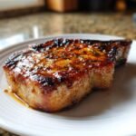 Nahaufnahme eines saftigen Delicious Brown Sugar Pork Chop auf einem wei&szlig;en Teller, glasiert und mit Kr&auml;utern bestreut.