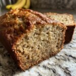 Nahaufnahme eines aufgeschnittenen, saftigen Bananenbrots, das auf einer Marmorarbeitsplatte liegt. Perfekt f&uuml;r ein einfaches Bananenbrot Rezept.