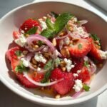 Nahaufnahme eines erfrischenden Erdbeer-Feta-Salats mit roten Zwiebeln, Minze und Pinienkernen.