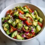 Nahaufnahme eines erfrischenden Gurken-Tomaten-Avocado-Salats in einer wei&szlig;en Sch&uuml;ssel, garniert mit Kr&auml;utern.