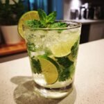 Ein Glas mit einem erfrischenden Kokos-Mojito, gef&uuml;llt mit Eis, Limettenscheiben und Minzbl&auml;ttern.