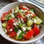 Nahaufnahme eines erfrischenden Tomaten Feta Gurkensalats in einer wei&szlig;en Sch&uuml;ssel, garniert mit Kr&auml;utern.