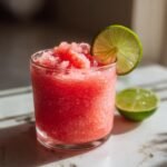 Ein Glas mit einem erfrischenden Wassermelonen-Slushie, garniert mit einer Limettenscheibe.