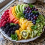 Eine bunte Obstplatte mit frischen Fr&uuml;chten wie Wassermelone, Beeren, Kiwi und Trauben, garniert mit Minze.