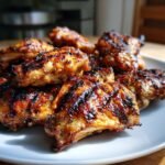 Nahaufnahme von saftigen, gegrillten H&auml;hnchenfl&uuml;geln mit Grillstreifen auf einem wei&szlig;en Teller, perfekt f&uuml;r Sommerrezepte.