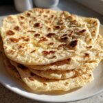 Nahaufnahme von gestapelten, frisch gebackenen Weizen Tortillas auf einem wei&szlig;en Teller mit leichten R&ouml;ststellen.