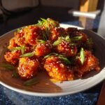 Nahaufnahme von hausgemachten Orange Chicken Bites, glasiert und mit Sesam und Fr&uuml;hlingszwiebeln garniert.