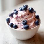 Nahaufnahme eines k&ouml;stlichen Blaubeer-Frischk&auml;se-Aufstrichs, garniert mit frischen Blaubeeren.