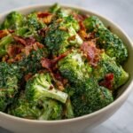 Nahaufnahme eines knackigen Brokkolisalats mit cremiger So&szlig;e, knusprigem Speck und Sonnenblumenkernen in einer Sch&uuml;ssel.