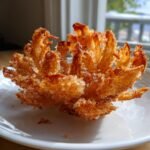 Nahaufnahme einer knusprigen Blooming Onion, zubereitet im Air Fryer, auf einem wei&szlig;en Teller.