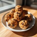 Ein Teller mit leckeren Erdnussbutter-Proteinb&auml;llchen, verziert mit Schokost&uuml;ckchen und Haferflocken.