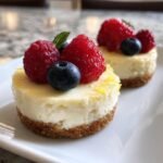 Zwei Low-Sugar Mini Greek Yogurt Cheesecakes, garniert mit Himbeeren, Blaubeeren und Minze.