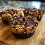 Drei No-Bake Peanut Butter Oat Cups mit Schokostreuseln auf einem Holzbrett.