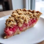 Ein St&uuml;ck perfekt s&uuml;&szlig;er Rhabarberkuchen mit knuspriger Krume auf einem wei&szlig;en Teller.