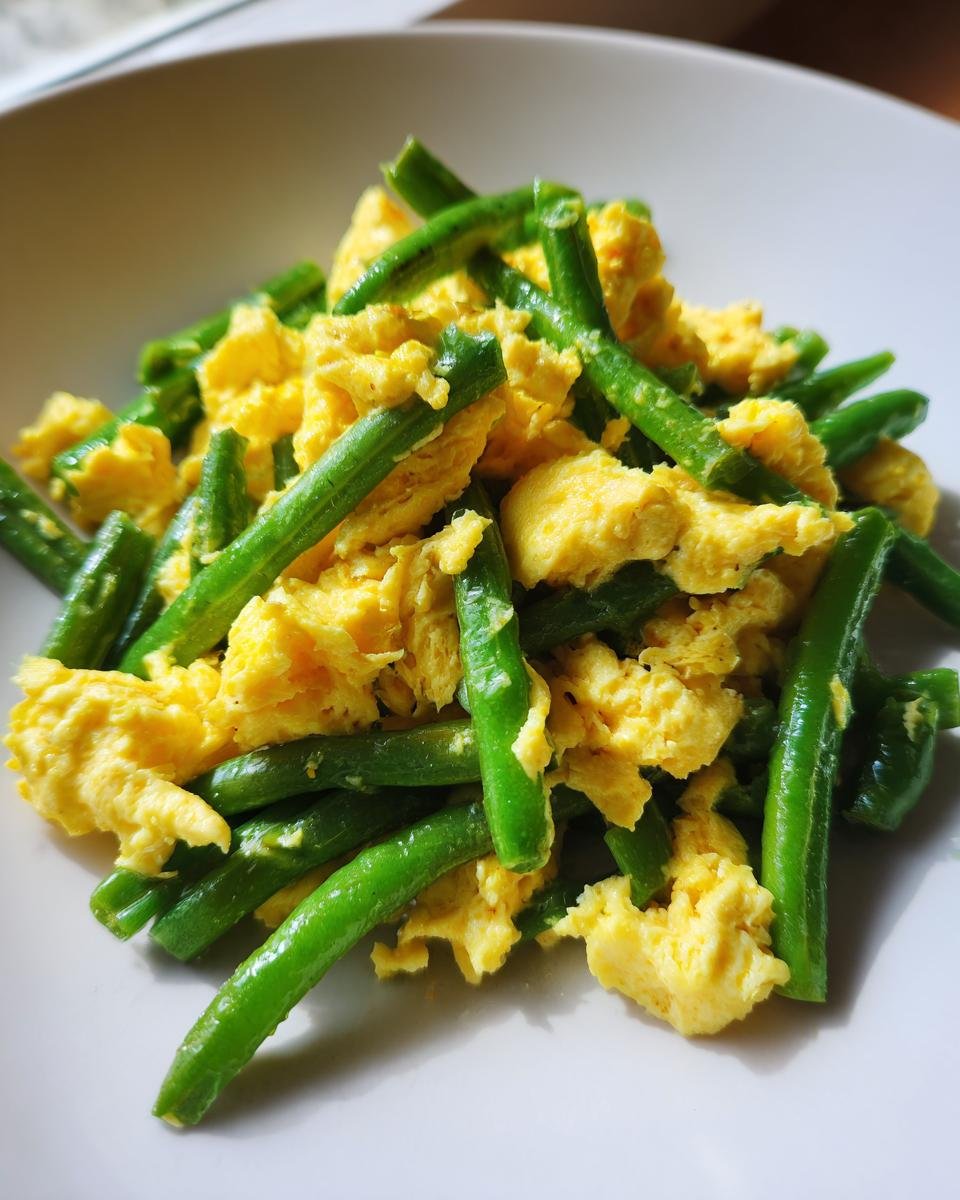 Nahaufnahme von R&uuml;hrei mit gebratenen gr&uuml;nen Bohnen auf einem Teller.