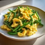 Nahaufnahme von R&uuml;hrei mit gebratenen gr&uuml;nen Bohnen auf einem Teller.