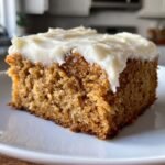 Ein St&uuml;ck saftiger Bananenriegel mit cremigem Frischk&auml;se-Frosting auf einem wei&szlig;en Teller.