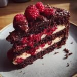 Ein St&uuml;ck Schokoladen-Himbeer-Kuchen mit drei Schichten dunklem Schokoladenkuchen, Himbeerf&uuml;llung und Sahne.