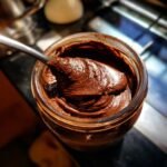 Ein L&ouml;ffel voller selbstgemachter Nutella, cremig und gl&auml;nzend, aus einem Glas gesch&ouml;pft.