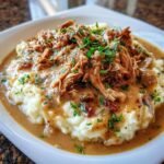 Ein Teller mit cremigem Kartoffelp&uuml;ree, &uuml;bergossen mit zartem Slow Cooker H&auml;hnchen und So&szlig;e, garniert mit Petersilie.