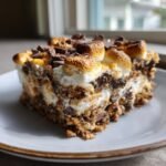 Ein St&uuml;ck S'mores Lasagne auf einem Teller mit geschmolzenen Marshmallows und Schokoladenst&uuml;ckchen.
