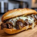 Nahaufnahme eines saftigen Philly Cheesesteak mit geschmolzenem K&auml;se und karamellisierten Zwiebeln auf einem Br&ouml;tchen.