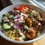 Nahaufnahme einer unwiderstehlichen griechischen H&auml;hnchen-Bowl mit Quinoa, H&auml;hnchenst&uuml;cken, Gurken, Tomaten, roten Zwiebeln, Oliven und Feta.