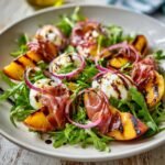 Nahaufnahme eines unwiderstehlichen gegrillten Nektarinen Burrata Prosciutto Salats mit Rucola, gegrillten Nektarinen, Burrata-Kugeln und Prosciutto.