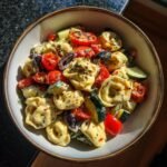 Nahaufnahme eines Sch&uuml;ssel mit unwiderstehlichem Tortellini-Nudelsalat, garniert mit Kirschtomaten, Gurken und Oliven.