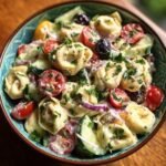 Nahaufnahme eines Sch&uuml;ssel mit unwiderstehlichem Tortellini Nudelsalat, belegt mit Tomaten, Gurken, Zwiebeln und Petersilie.
