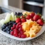 Eine wei&szlig;e Platte mit einer bunten Mischung aus 4. Juli Obstplatte Sommer Spa&szlig;: Erdbeeren, Blaubeeren, Himbeeren, Brombeeren, Melonenst&uuml;cken und Melonensternen.