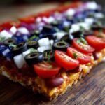 Nahaufnahme eines American Flag Layered Taco Dips mit Tomaten, schwarzen Oliven und Zwiebeln.