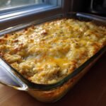 &Uuml;berbackener Chicken Cauliflower Rice Casserole mit goldbrauner K&auml;sekruste in einer Glasform.