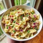 Nahaufnahme einer Sch&uuml;ssel mit Chilled 4th Of July Pasta Salad, bestehend aus Farfalle-Nudeln, Erbsen, Speck und roten Zwiebeln.