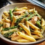 Nahaufnahme einer Sch&uuml;ssel mit cremiger H&auml;hnchen-Spargel-Penne, garniert mit Kr&auml;utern.