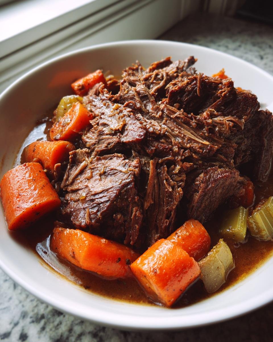 Ein Teller mit zartem Dutch Oven Pot Roast, geschmort mit großen Karottenstücken in dunkler Soße.