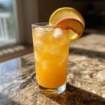 Ein Glas erfrischende Pfirsich-Limonade mit Eisw&uuml;rfeln, garniert mit einer Zitronen- und Pfirsichscheibe.