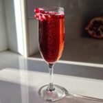 Ein funkelnder Pomegranate Mimosa in einem Sektglas, garniert mit Granatapfelkernen.