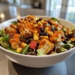 Nahaufnahme eines Southwest Chicken Salad mit gegrillten H&auml;hnchenst&uuml;cken, Mais, schwarzen Bohnen und roter So&szlig;e.