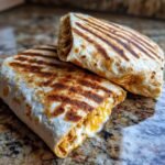 Zwei gegrillte Burritos mit geschmolzenem K&auml;se, die auf einer Marmorarbeitsplatte liegen.