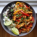 Eine Sch&uuml;ssel mit Flavorful Chicken Fajita Rice Bowl, garniert mit Limettenspalten und Koriander.
