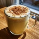 Nahaufnahme eines Glases mit cremigem, gelbem Homemade Eggnog, gekr&ouml;nt mit Milchschaum und Zimt.