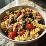 Nahaufnahme von Griechischem H&auml;hnchen-Nudel-Salat mit Fusilli-Nudeln, H&auml;hnchenbrust, Kirschtomaten und schwarzen Oliven, garniert mit Petersilie.