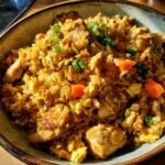 Sch&uuml;ssel mit H&auml;hnchenreis, garniert mit Fr&uuml;hlingszwiebeln und Karottenst&uuml;cken.