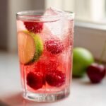 Nahaufnahme eines Glases Honey Sweetened Cherry Limeade mit frischen Kirschen, Limettenscheiben und Eisw&uuml;rfeln.