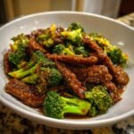Nahaufnahme von saftigem Instant Pot Beef And Broccoli mit gl&auml;nzender So&szlig;e in einer wei&szlig;en Sch&uuml;ssel.